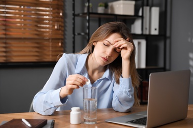 Woman putting medicine for hangover into glass of water in office
