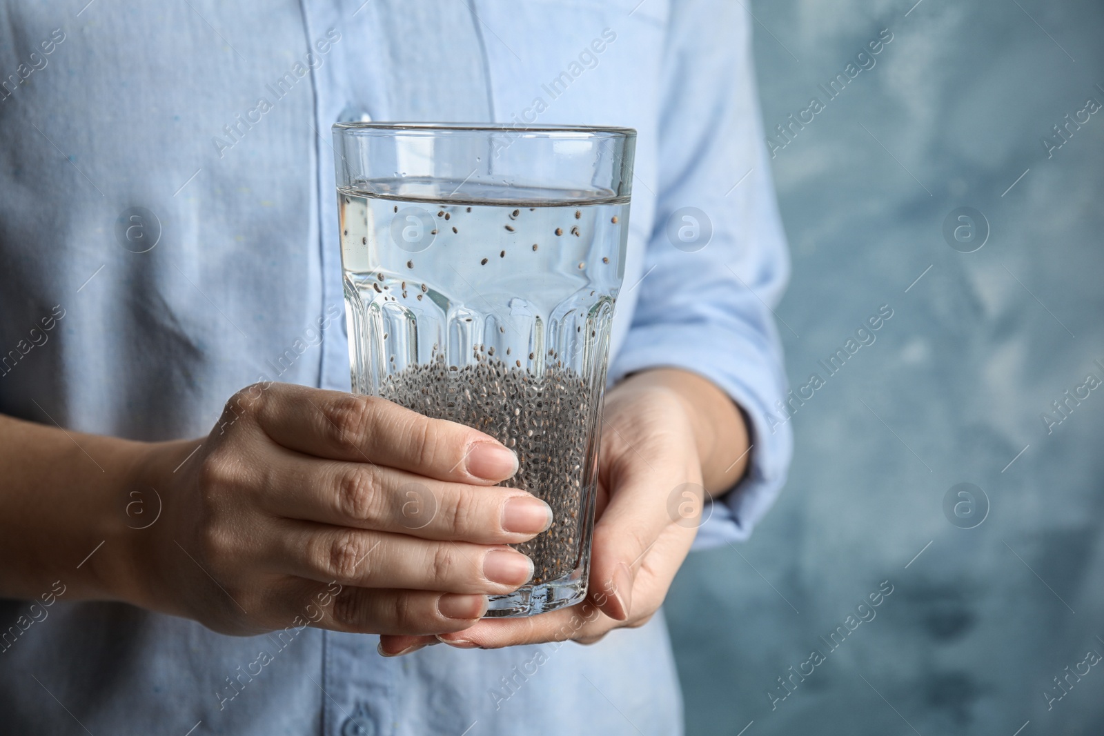 Photo of Woman holding glass of water with chia seeds on color background, closeup. Space for text