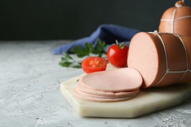 Delicious boiled sausage with tomatoes on grey textured table, closeup. Space for text