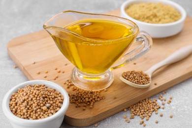 Photo of Jug of natural oil, mustard seeds and powder on light grey , closeup