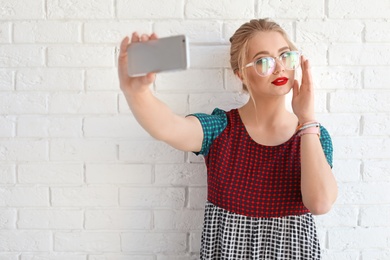 Attractive young woman taking selfie near brick wall