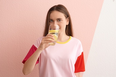 Young woman drinking lemon water on color background