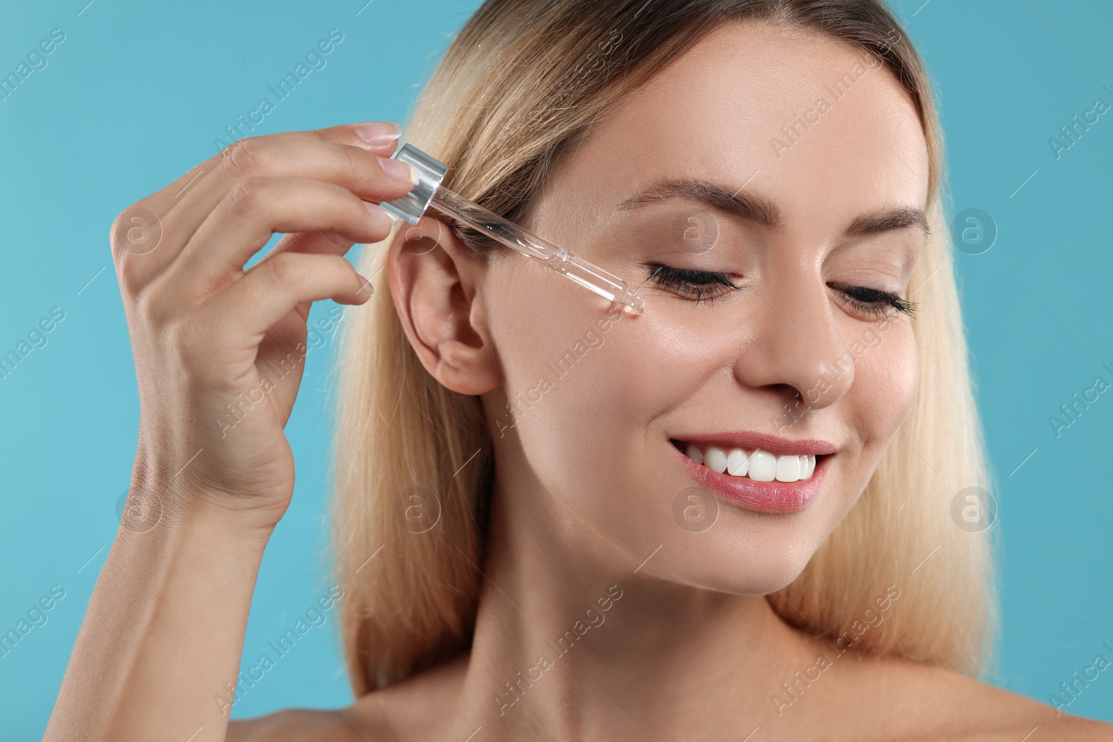 Photo of Beautiful woman applying cosmetic serum onto her face on light blue background, closeup