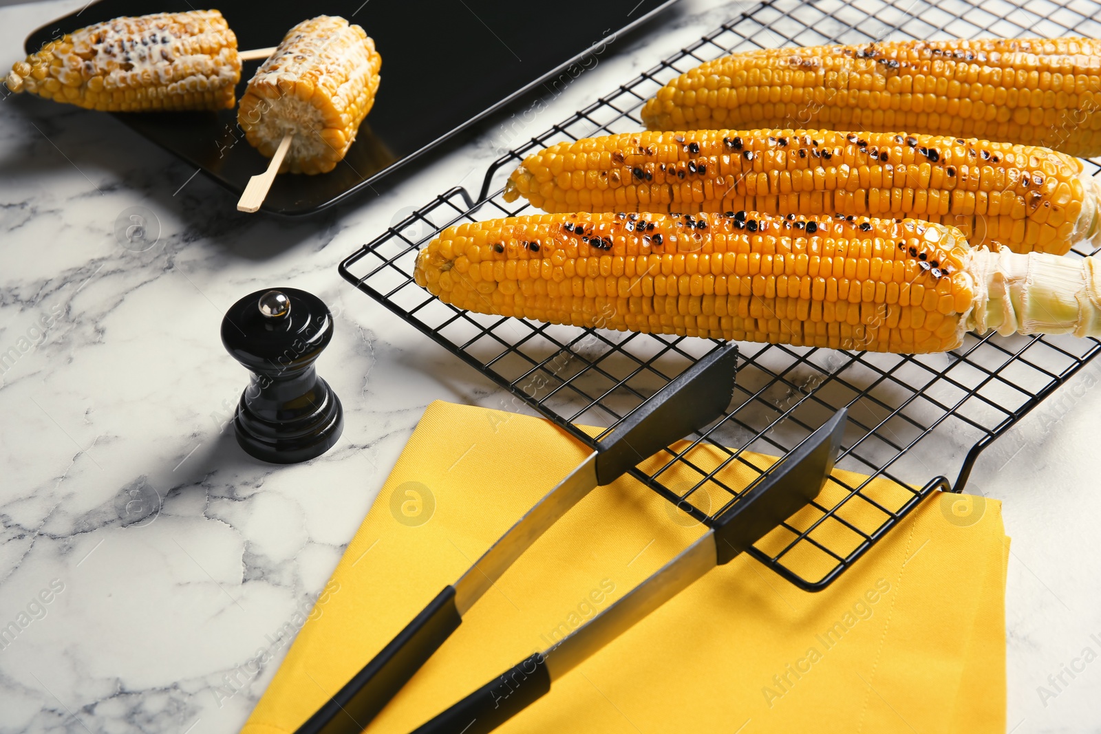 Photo of Cooling rack with grilled corn cobs on marble background