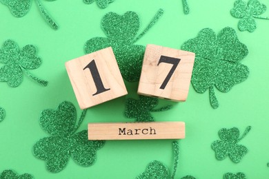 St. Patrick's day - 17th of March. Wooden block calendar and decorative clover leaves on green background, flat lay