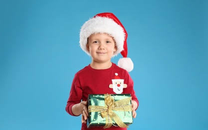 Photo of Cute child in Santa hat with Christmas gift on light blue background