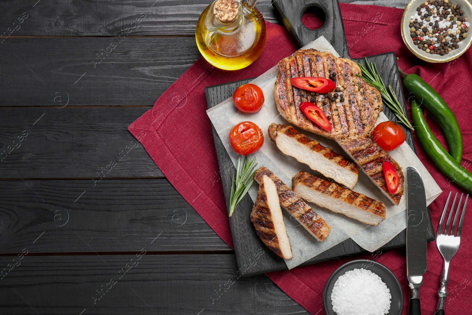 Photo of Grilled pork steaks with rosemary, spices, vegetables and cutlery on dark wooden table, top view. Space for text