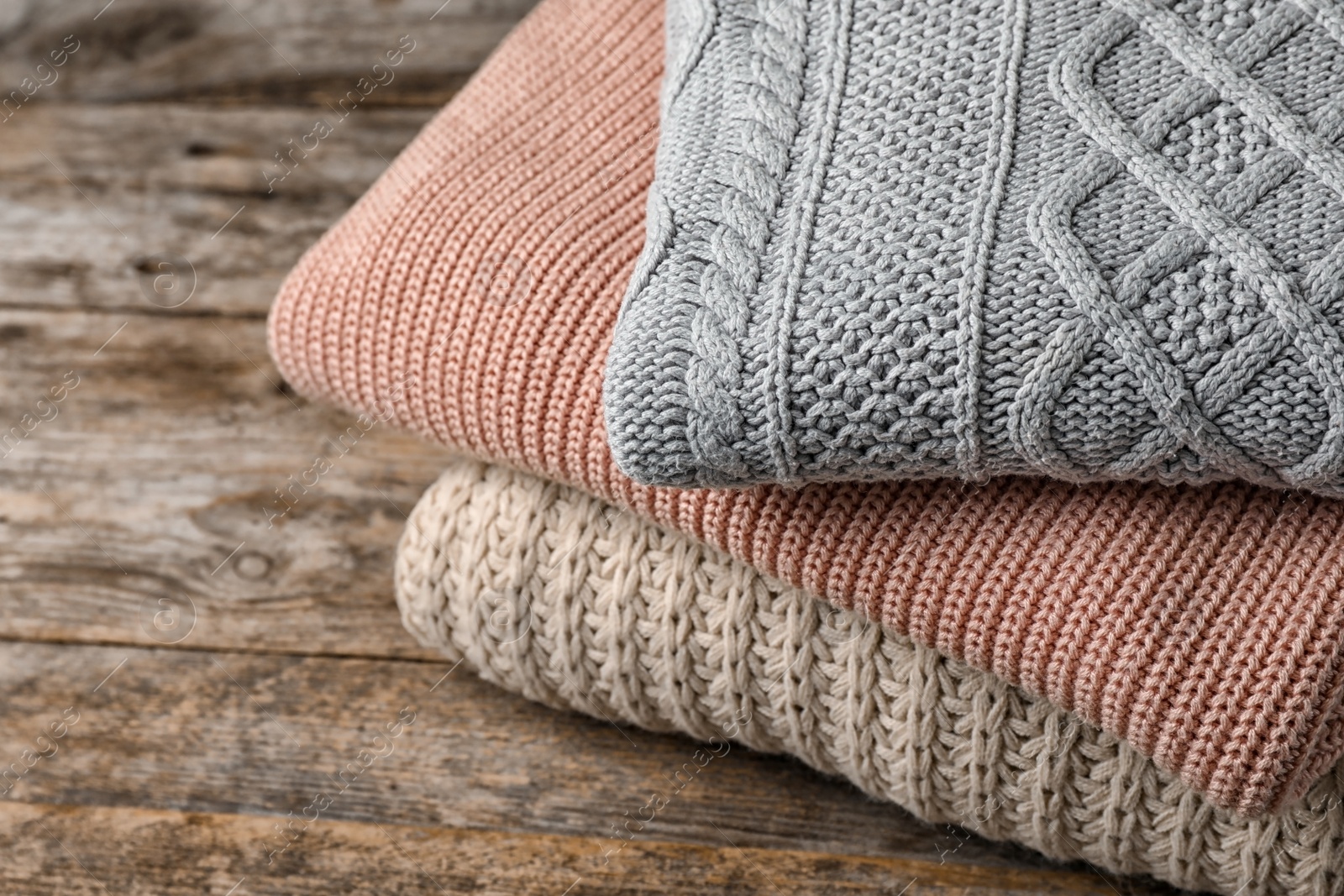 Photo of Stack of folded knitted sweaters on table, closeup