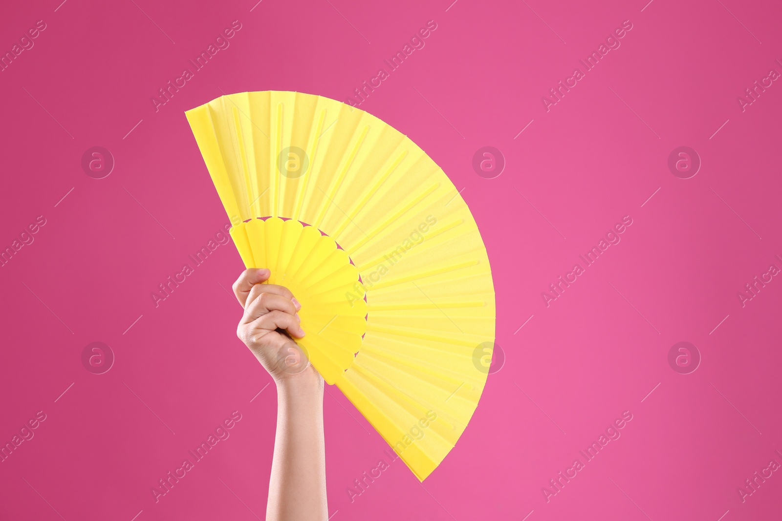 Photo of Woman holding yellow hand fan on pink background, closeup