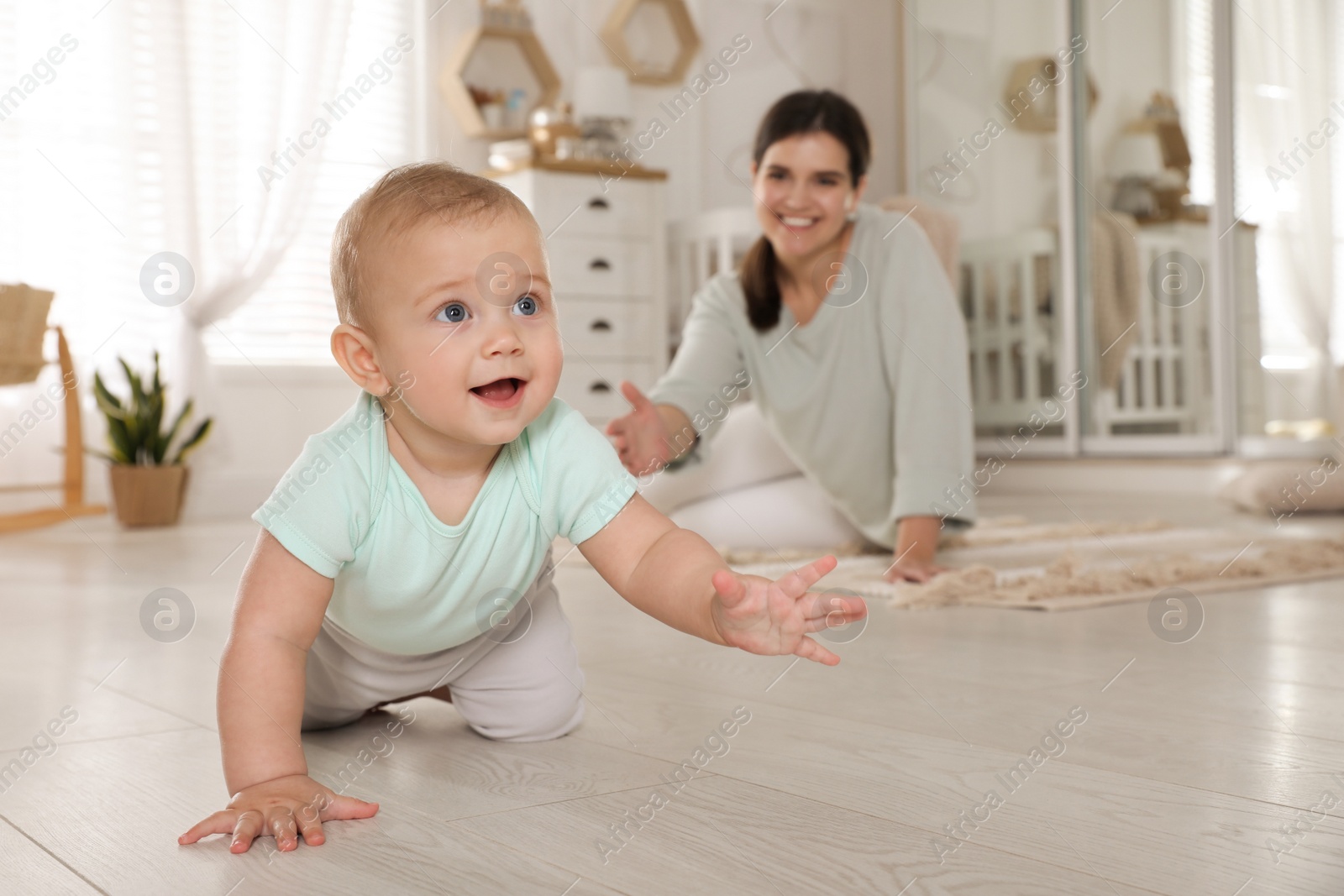 Photo of Happy young mother watching her cute baby crawl on floor at home