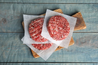 Photo of Raw meat cutlets for burger on blue wooden table, top view
