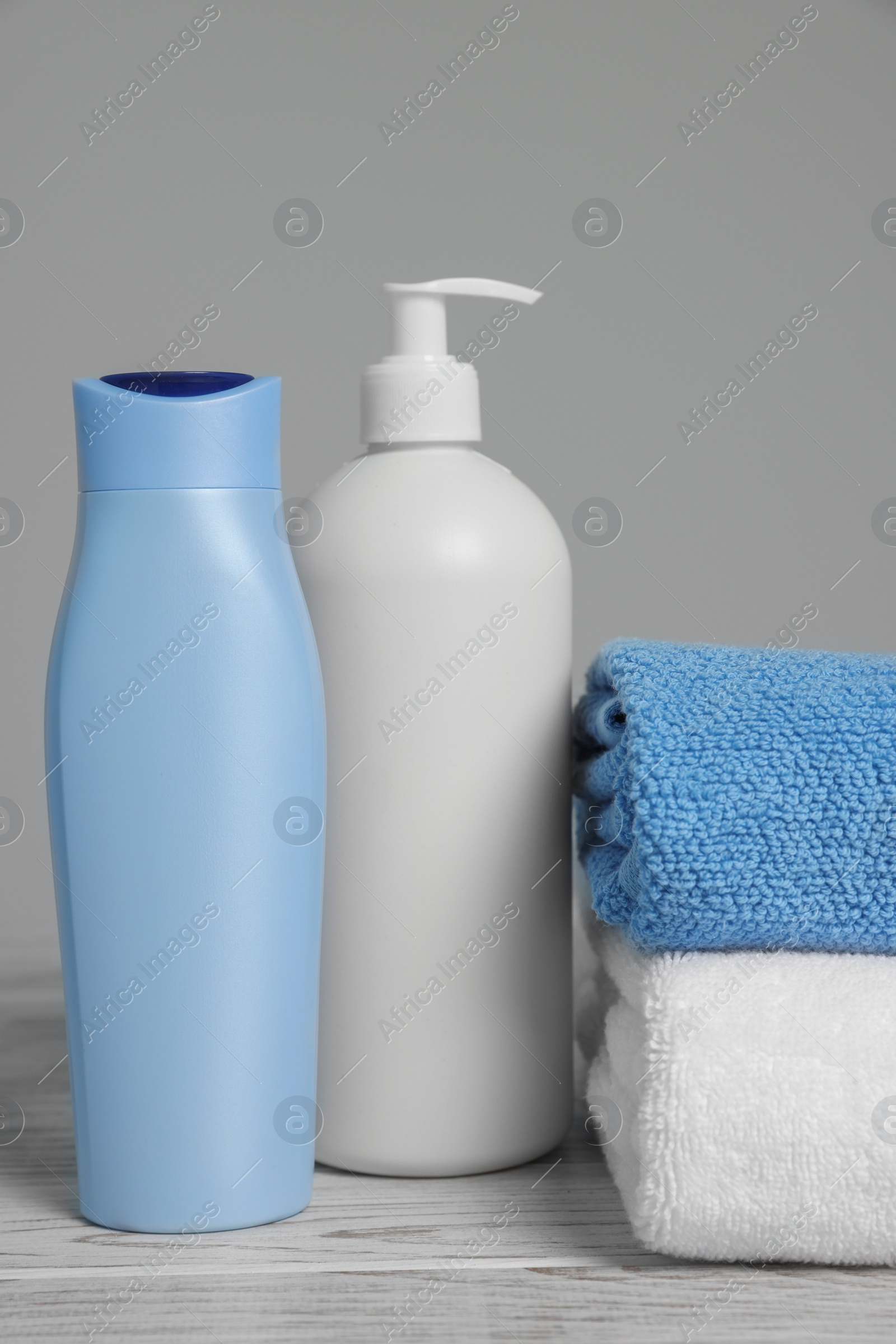 Photo of Soft folded towels with cosmetic products on white wooden table against light grey background