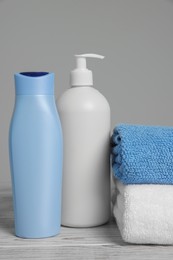 Soft folded towels with cosmetic products on white wooden table against light grey background