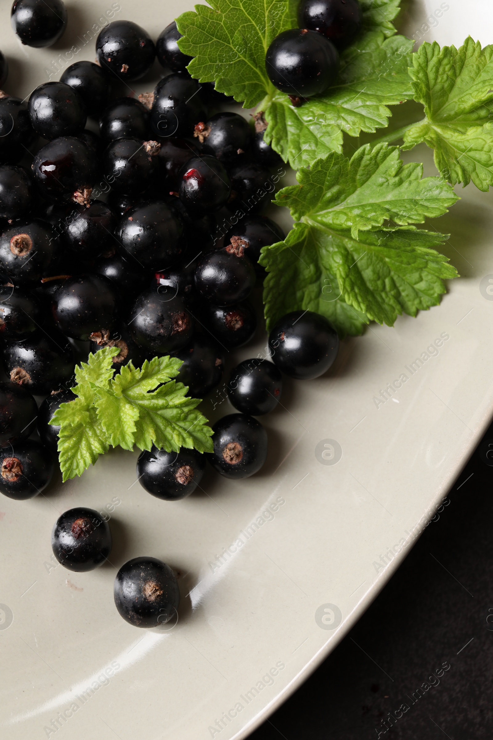 Photo of Plate with ripe blackcurrants and leaves on dark background, top view