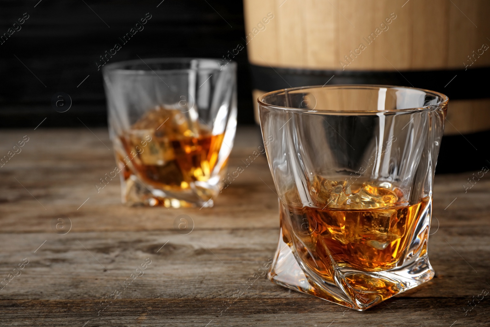Photo of Golden whiskey in glass with ice cubes on wooden table. Space for text