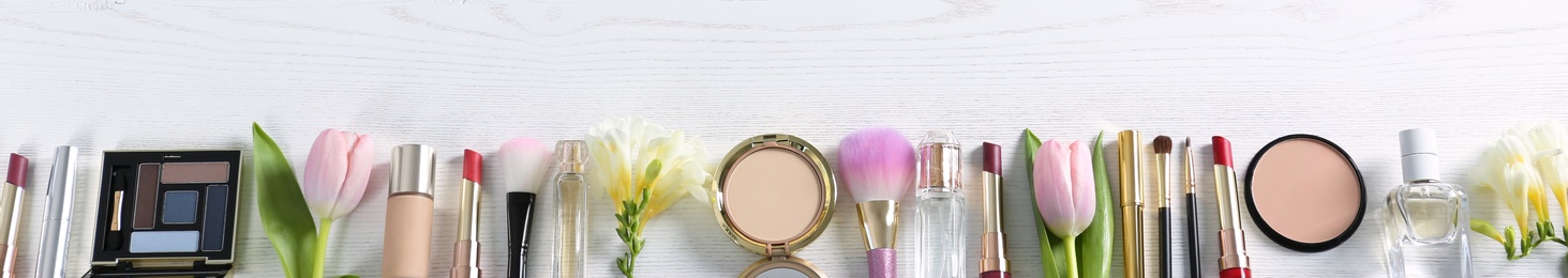 Photo of Flat lay composition with different decorative cosmetics and flowers on wooden table. Trendy makeup products