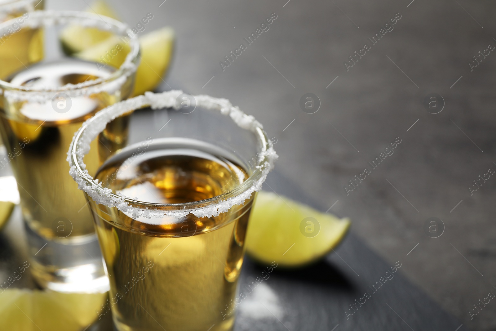 Photo of Mexican Tequila shots with salt and lime slices on grey table, closeup. Space for text