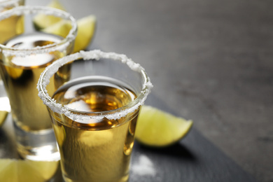 Mexican Tequila shots with salt and lime slices on grey table, closeup. Space for text