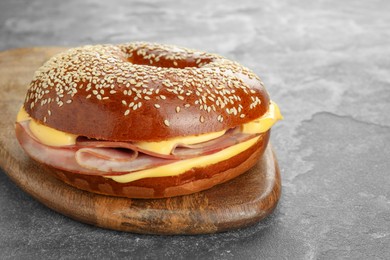 Delicious bagel with ham and cheese on grey textured table, space for text