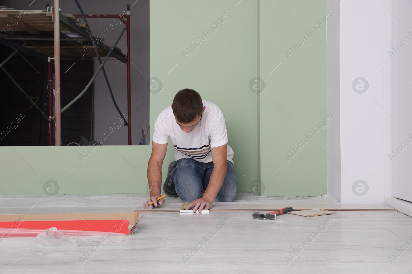 Photo of Man using pencil during installation of new laminate flooring in room