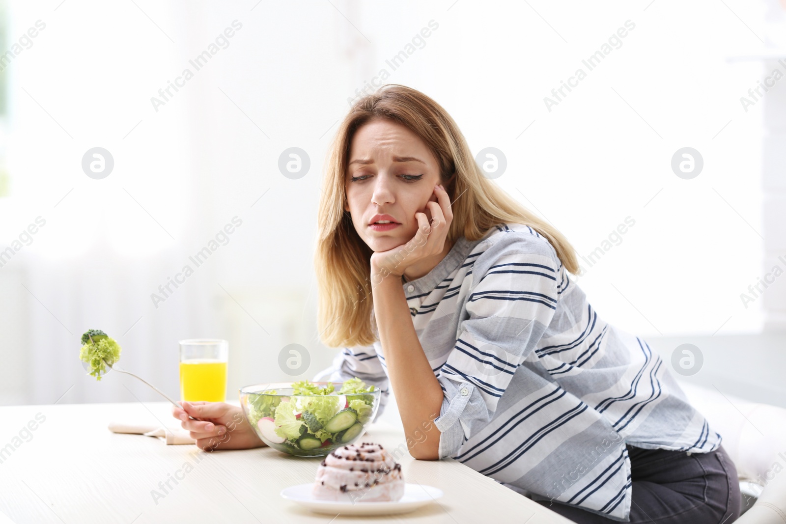 Photo of Unhappy woman choosing between vegetable salad and dessert in kitchen. Healthy diet