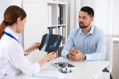 Orthopedist showing X-ray picture to patient at table in clinic