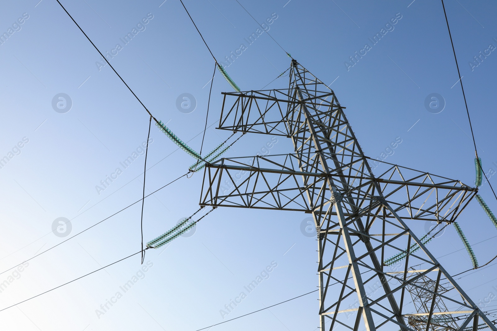 Photo of High voltage tower against blue sky on sunny day, low angle view