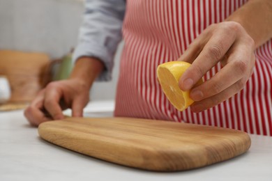 Photo of Man applying lemon juice on wooden cutting board at light table in kitchen, closeup