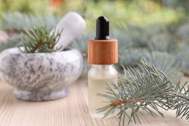 Photo of Pine essential oil and branches on white wooden table, closeup