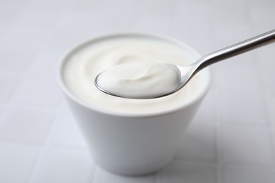 Photo of Eating delicious natural yogurt at white tiled table, closeup