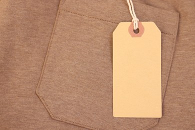 Photo of Cardboard tag on brown garment, top view. Space for text