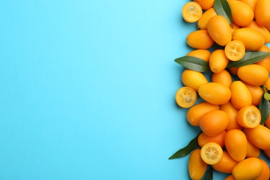 Photo of Fresh ripe kumquats with green leaves on light blue background, flat lay. Space for text