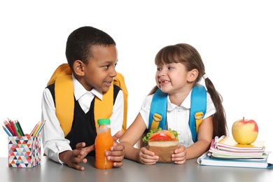 Photo of Schoolchildren with healthy food and backpacks sitting at table on white background