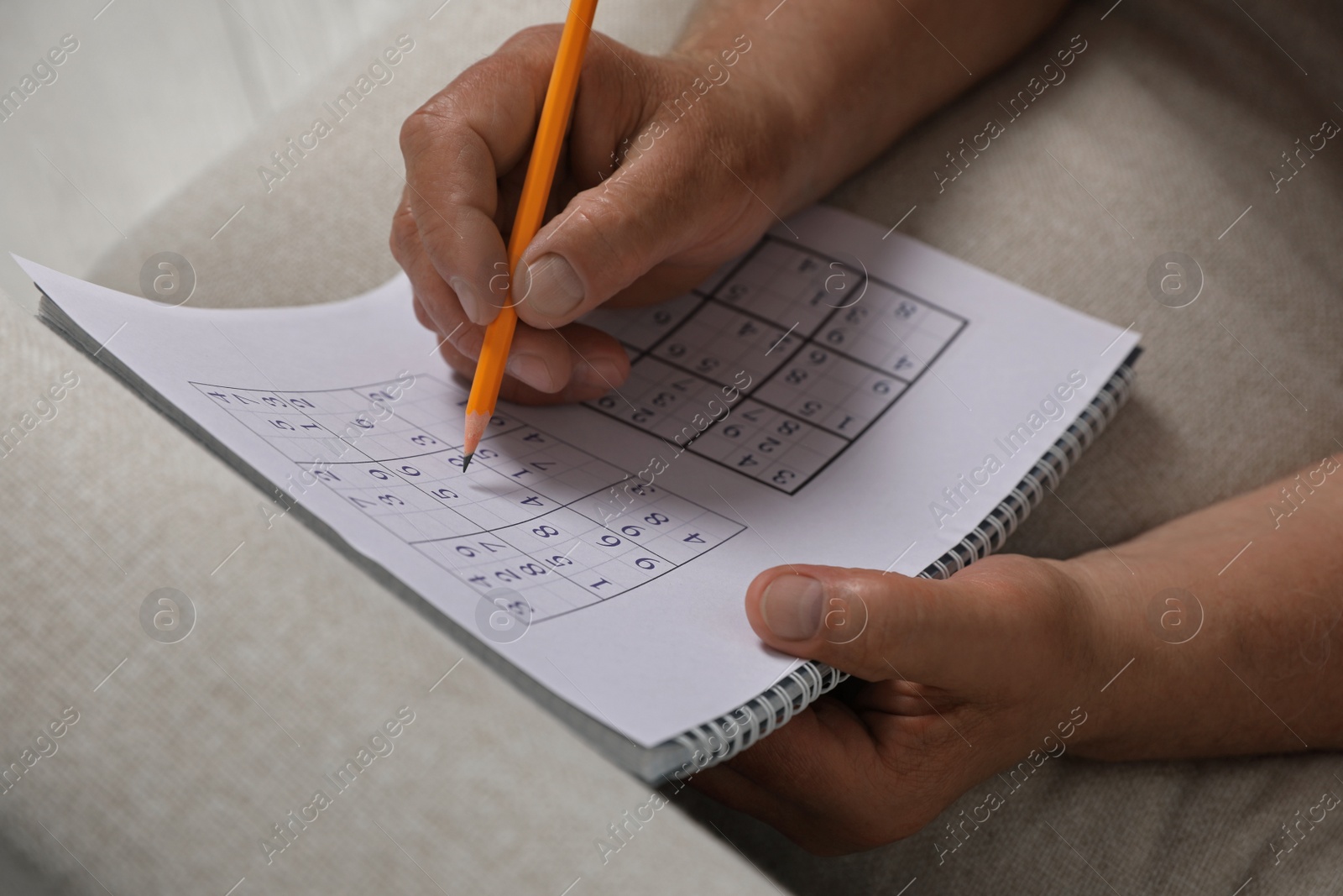 Photo of Senior man solving sudoku puzzle on sofa at home, closeup