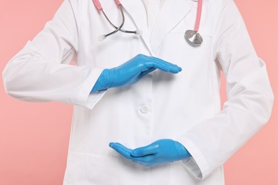 Doctor with stethoscope holding something on pink background, closeup