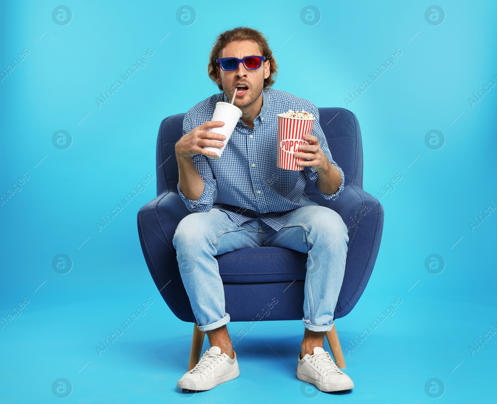 Photo of Emotional man with 3D glasses, popcorn and beverage sitting in armchair during cinema show on color background