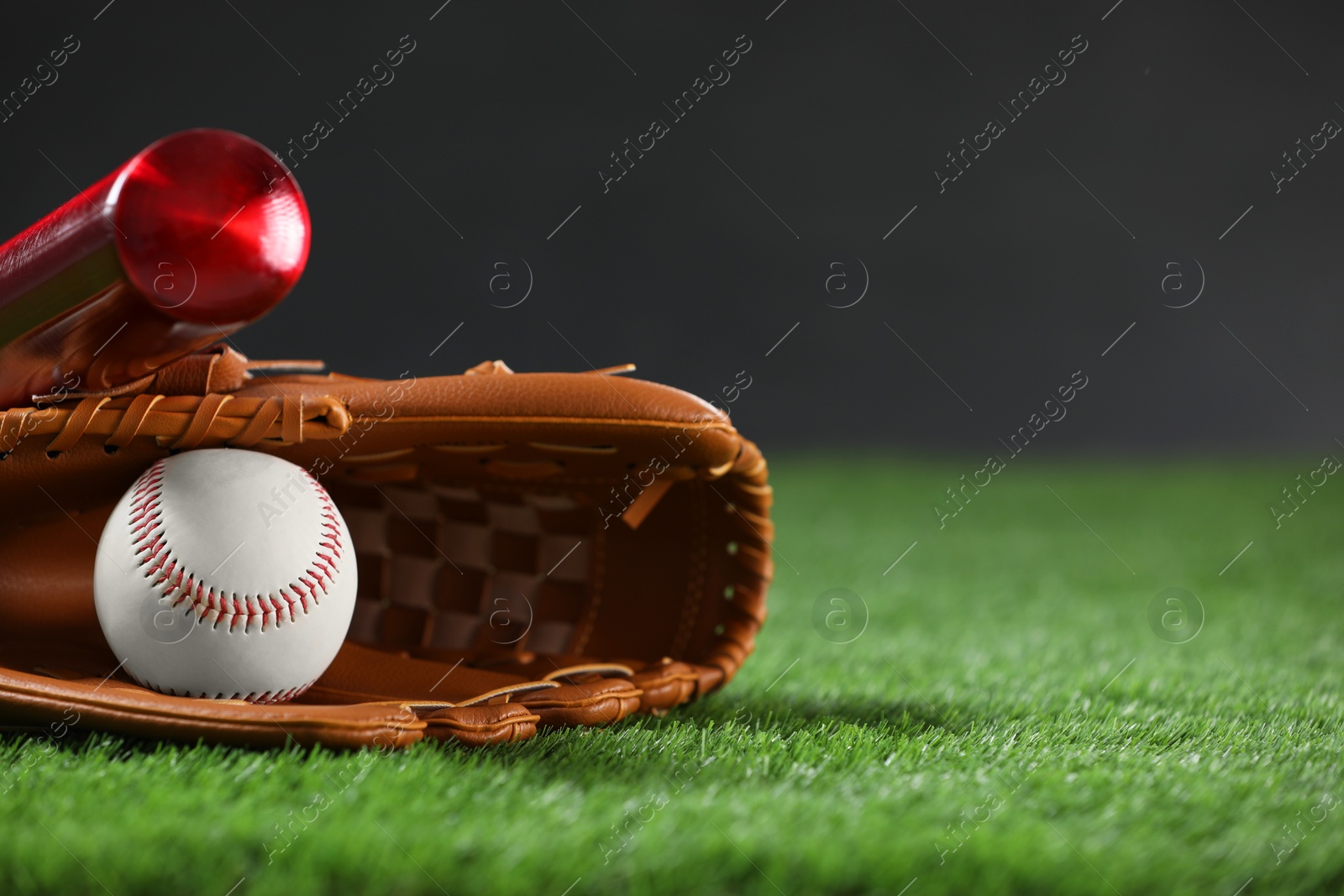 Photo of Baseball bat, leather glove and ball on green grass against dark background, closeup. Space for text