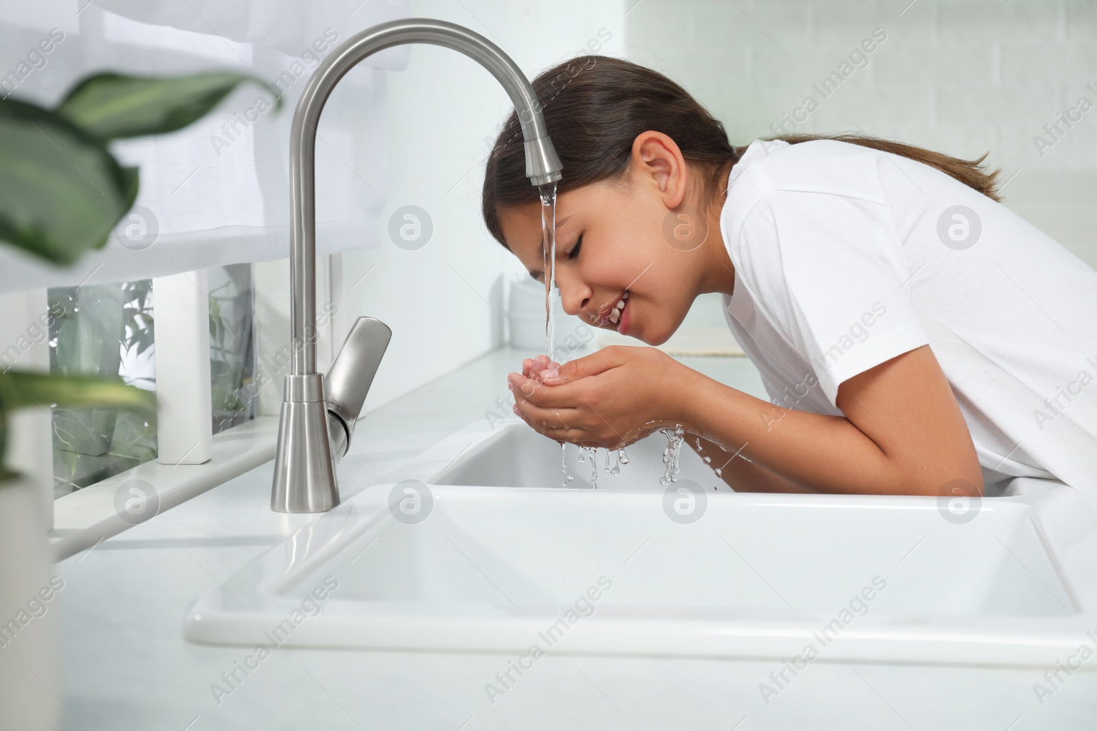 Photo of Girl drinking tap water over sink in kitchen