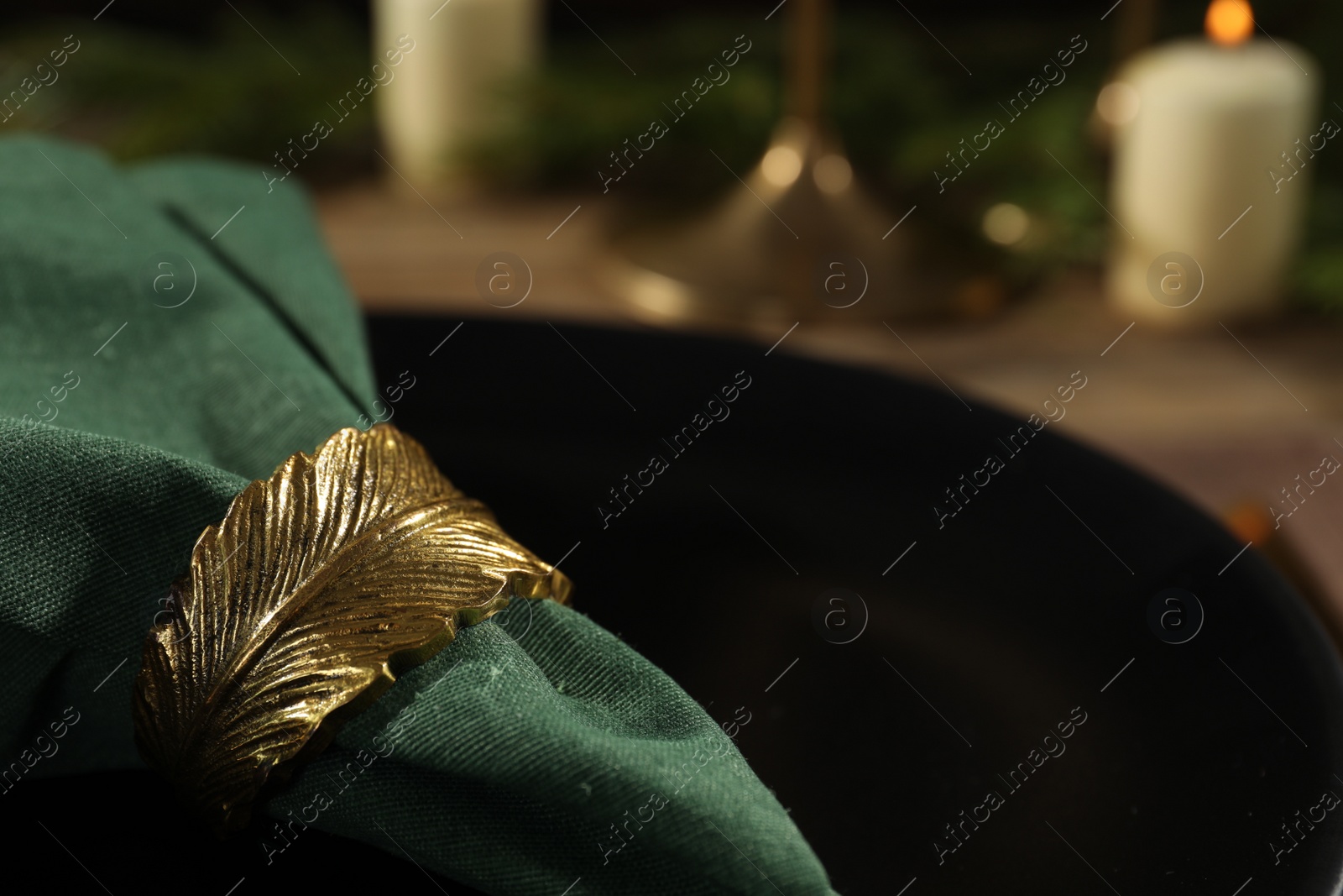 Photo of Green fabric napkin with beautiful decorative ring for table setting on black plate, closeup