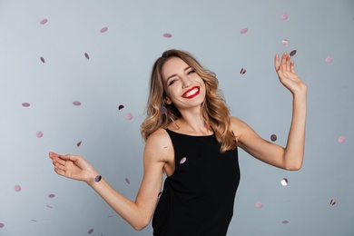 Happy young woman and confetti on grey background. Christmas celebration