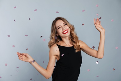 Photo of Happy young woman and confetti on grey background. Christmas celebration