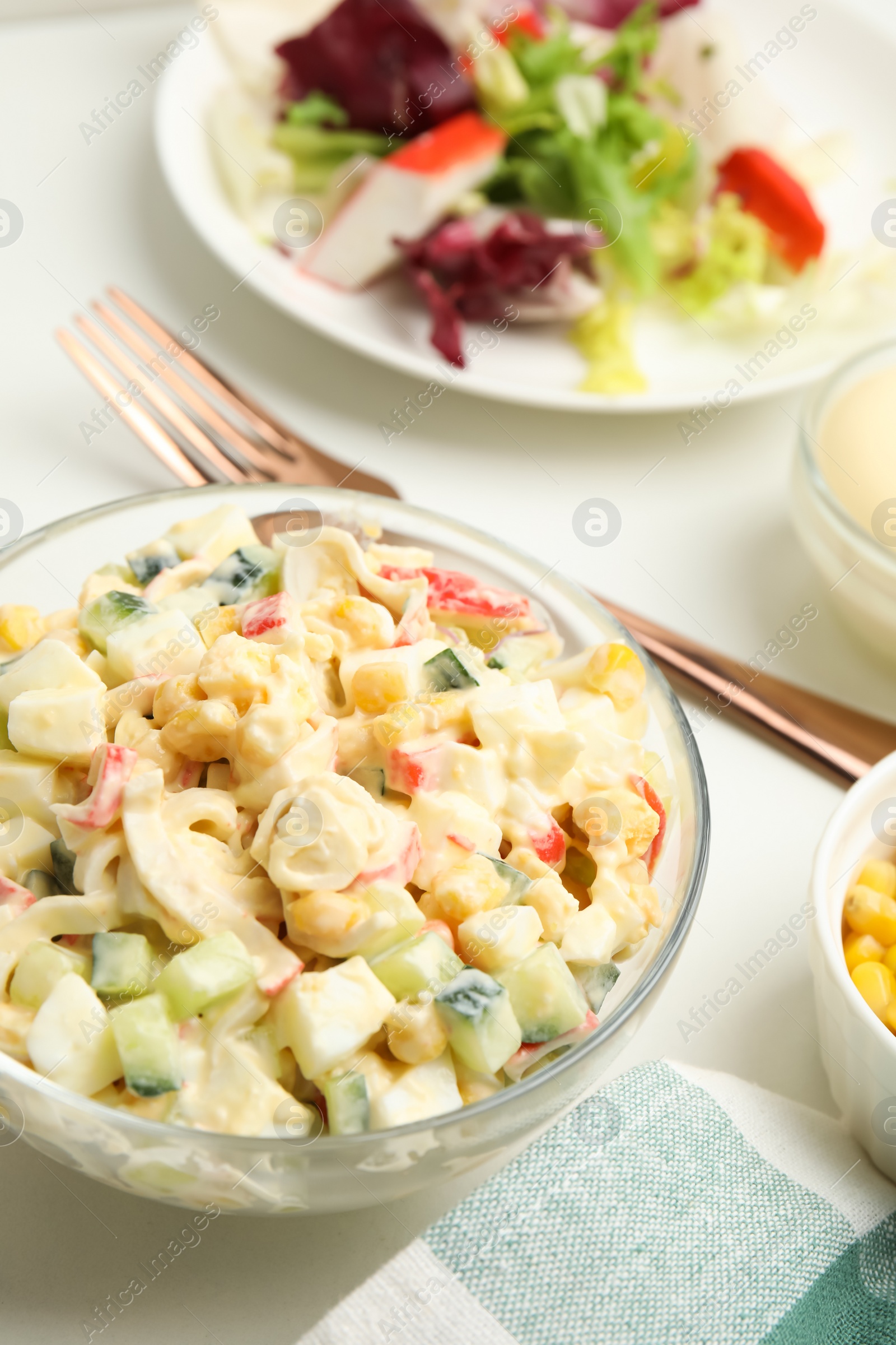 Photo of Delicious salad with fresh crab sticks in glass bowl on white table, closeup