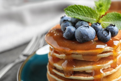 Delicious pancakes with fresh blueberries and syrup on table, closeup