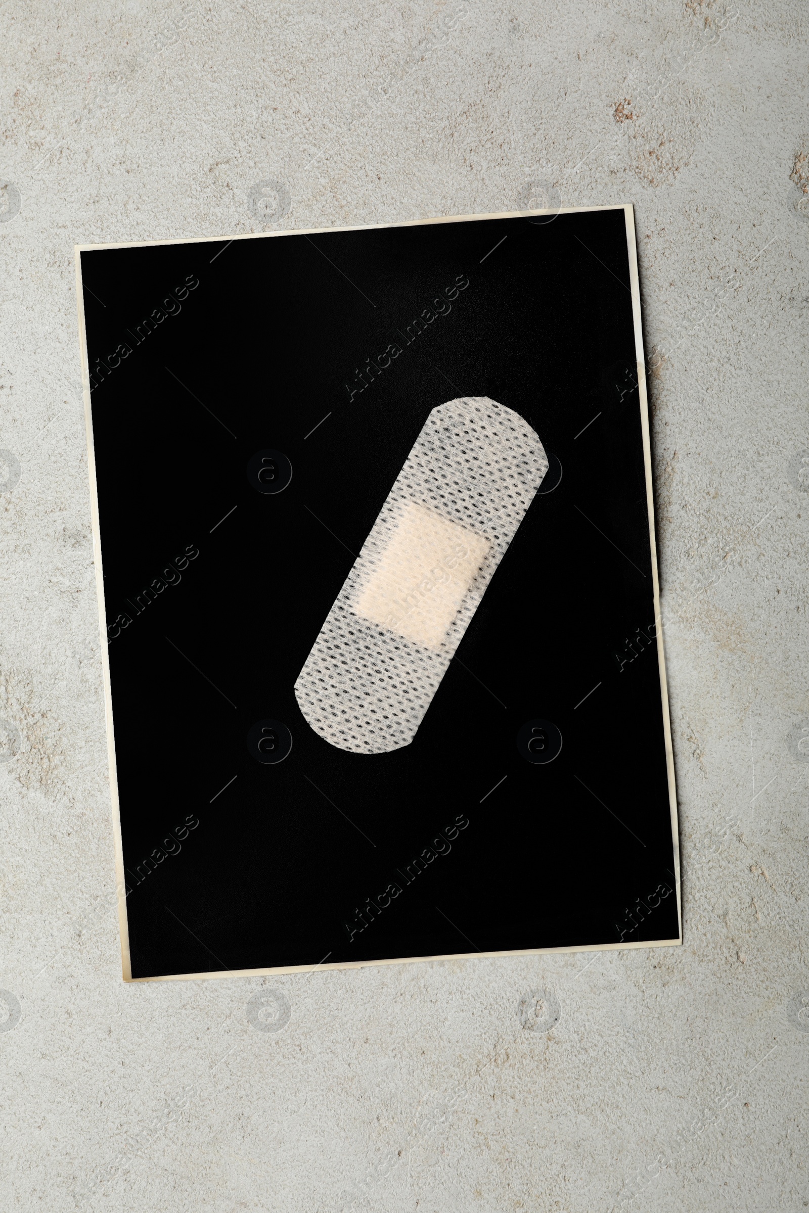 Photo of Black paper sheet with sticking plaster on light grey stone table, top view