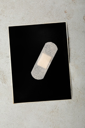 Photo of Black paper sheet with sticking plaster on light grey stone table, top view