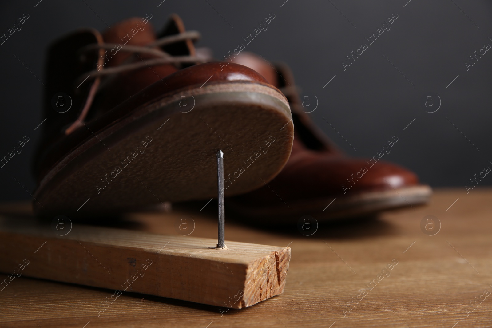 Photo of Metal nail in wooden plank and shoes on table, closeup