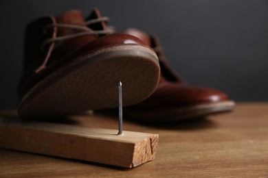 Photo of Metal nail in wooden plank and shoes on table, closeup