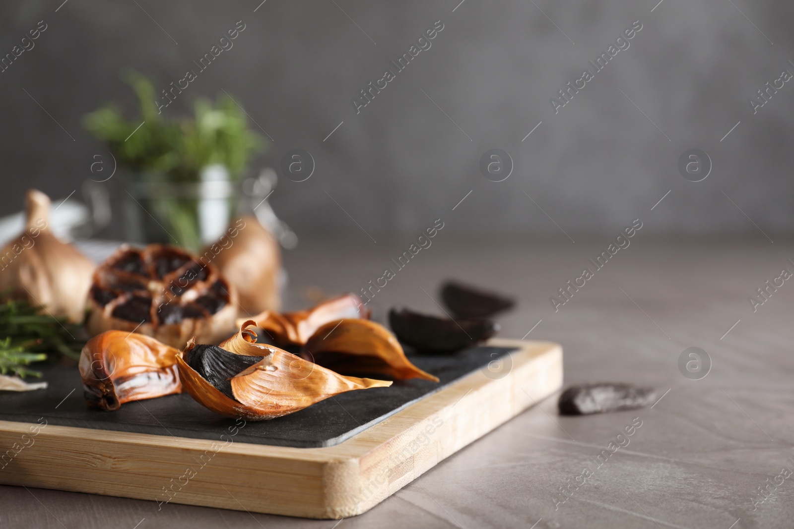 Photo of Board with black garlic on grey table. Space for text