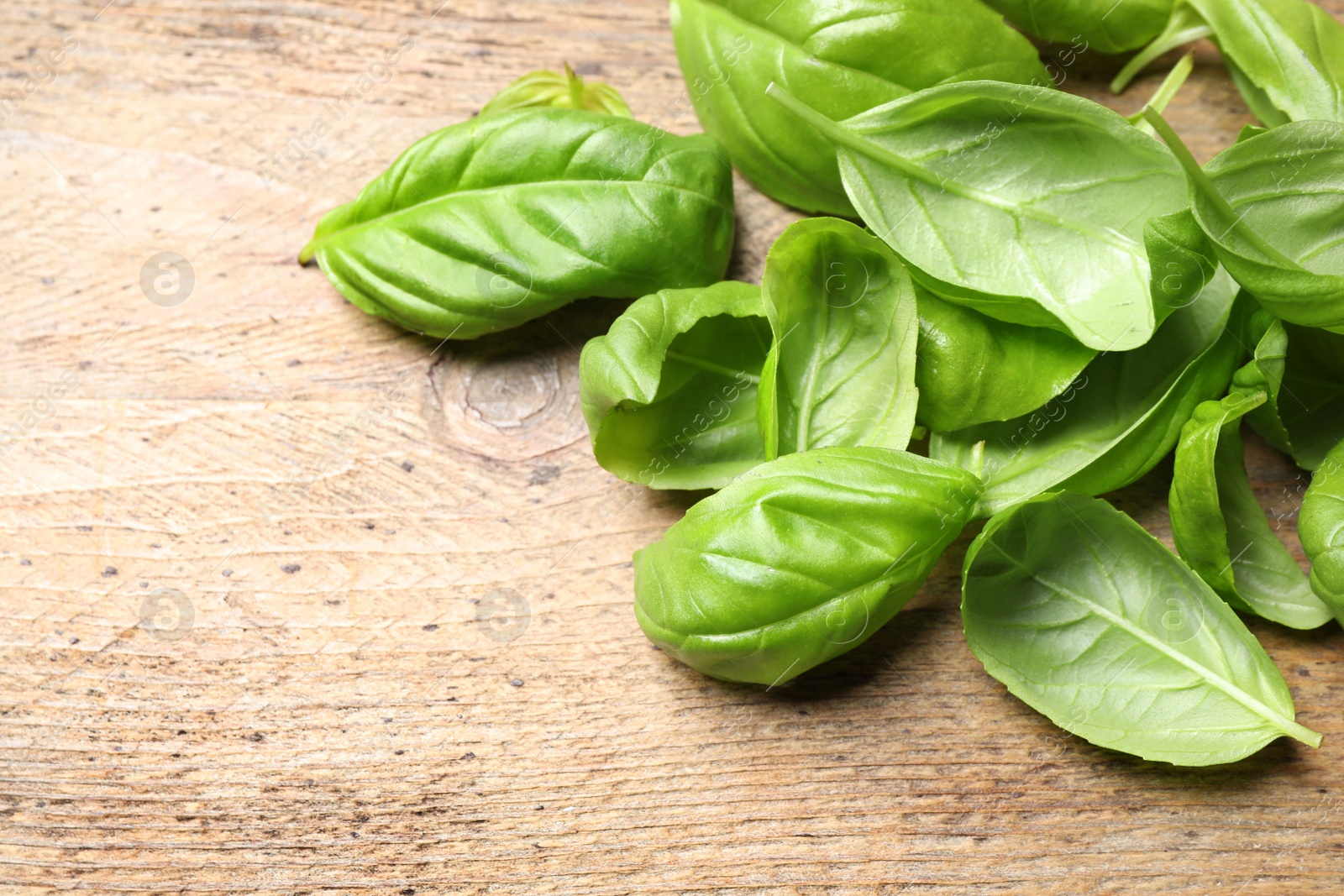 Photo of Fresh basil leaves on wooden table, closeup