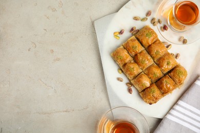 Photo of Delicious sweet baklava with pistachios and hot tea on light grey table, flat lay. Space for text